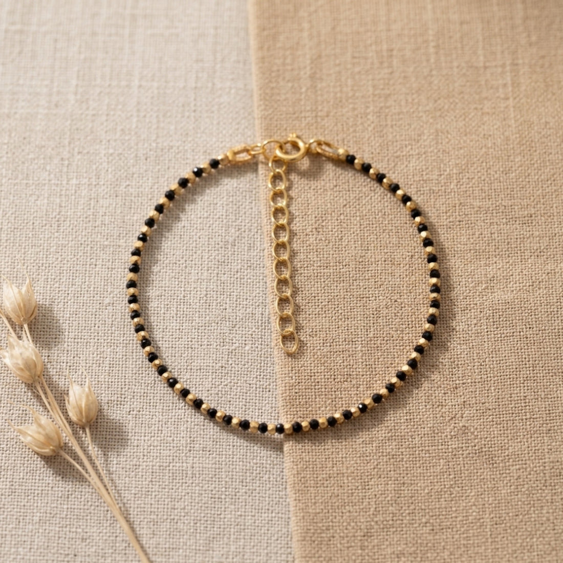 Pulsera Astra de ónix negro natural sobre plata de ley 925 dorada, extendida sobre lino