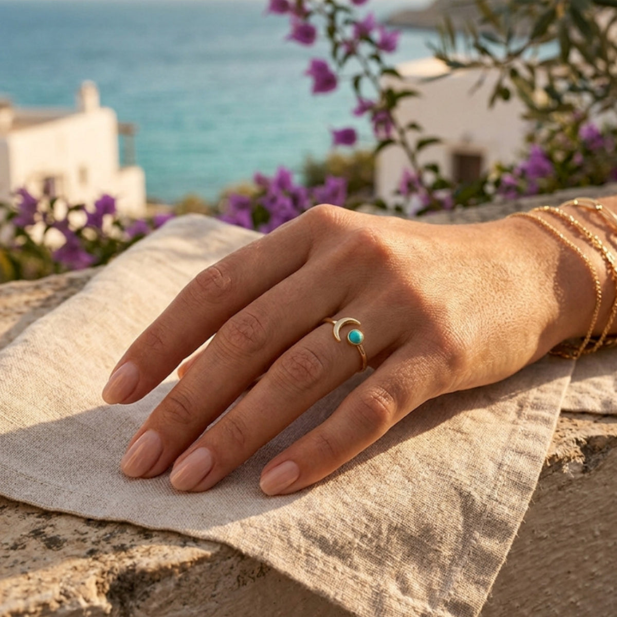 Anillo Aylin de turquesa en la mano, con el mar y buganvillas al fondo