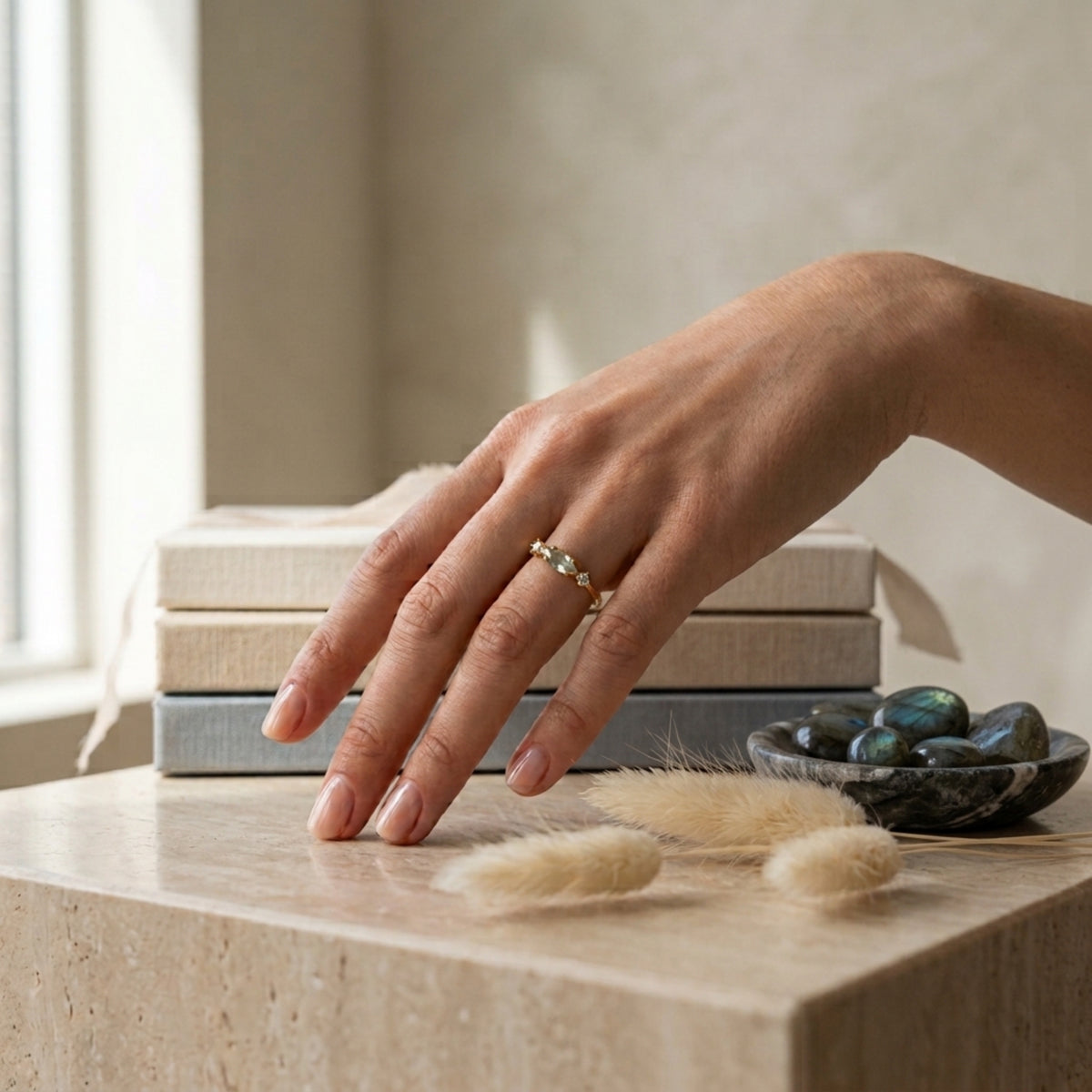 Mano sobre unos libros con el Anillo Nova, junto a piedras de labradorita en bruto