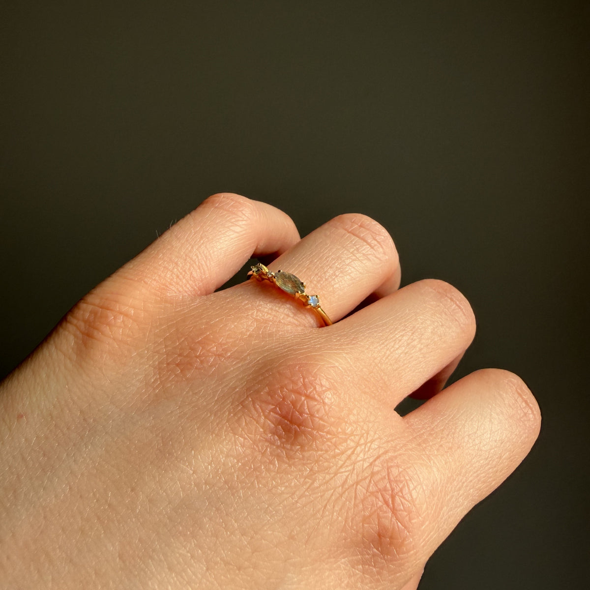 Anillo Nova de labradorita en la mano, iluminado sobre fondo oscuro