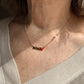 Detalle del Collar Mamá dorado sobre el escote, con su corazón rojo y la perla blanca