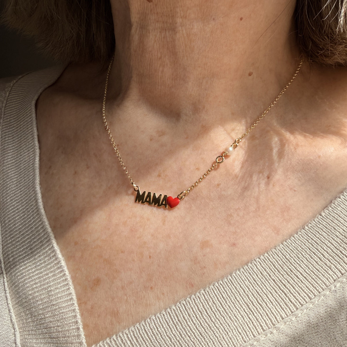 Detalle del Collar Mamá dorado sobre el escote, con su corazón rojo y la perla blanca