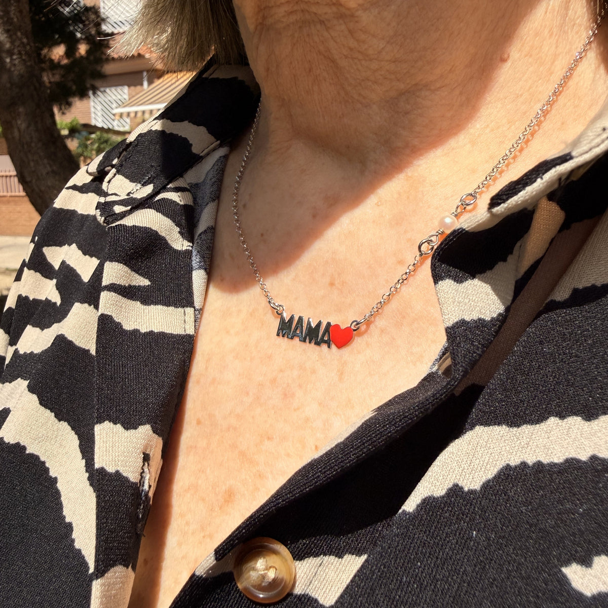 Collar Mamá plateado visto de cerca sobre una blusa estampada