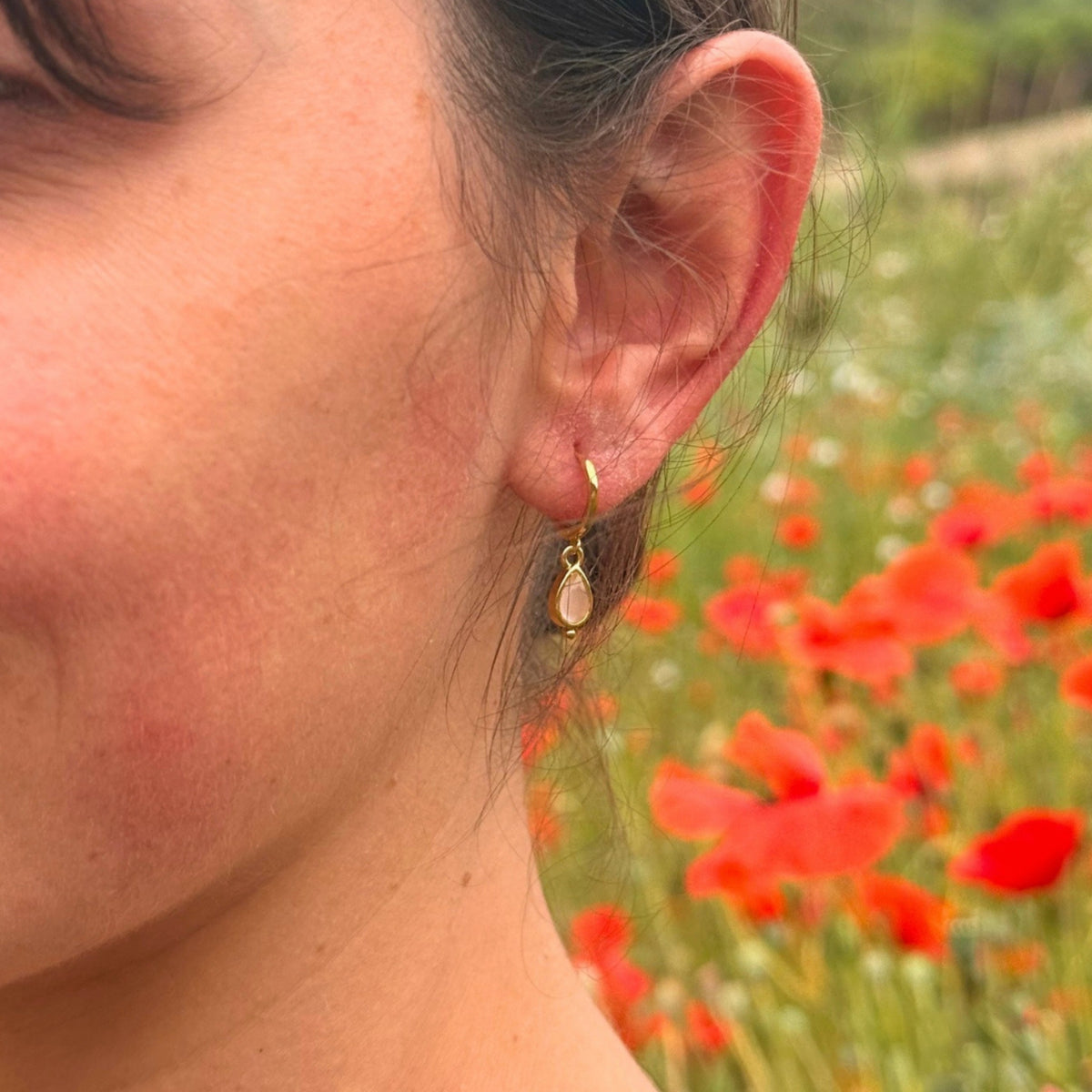 Pendiente Rosé de cuarzo rosa en la oreja, con amapolas al fondo