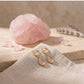 Pendientes Rosé de aro pequeño con cuarzo rosa natural, junto a un cuarzo rosa en bruto