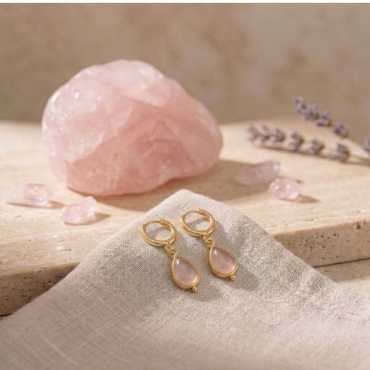 Pendientes Rosé de aro pequeño con cuarzo rosa natural, junto a un cuarzo rosa en bruto